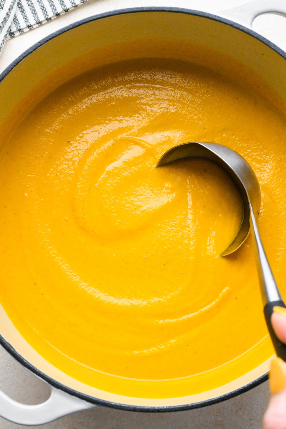 How to make Dairy Free Pumpkin Carrot Soup: A ladle dipping into the soup pot of soup.