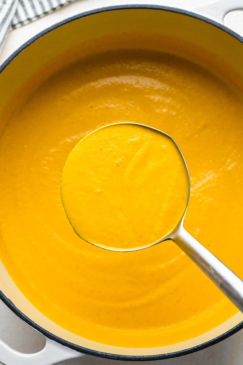 How to make Dairy Free Pumpkin Carrot Soup: A ladle lifting out a portion of the blended soup from soup pot.