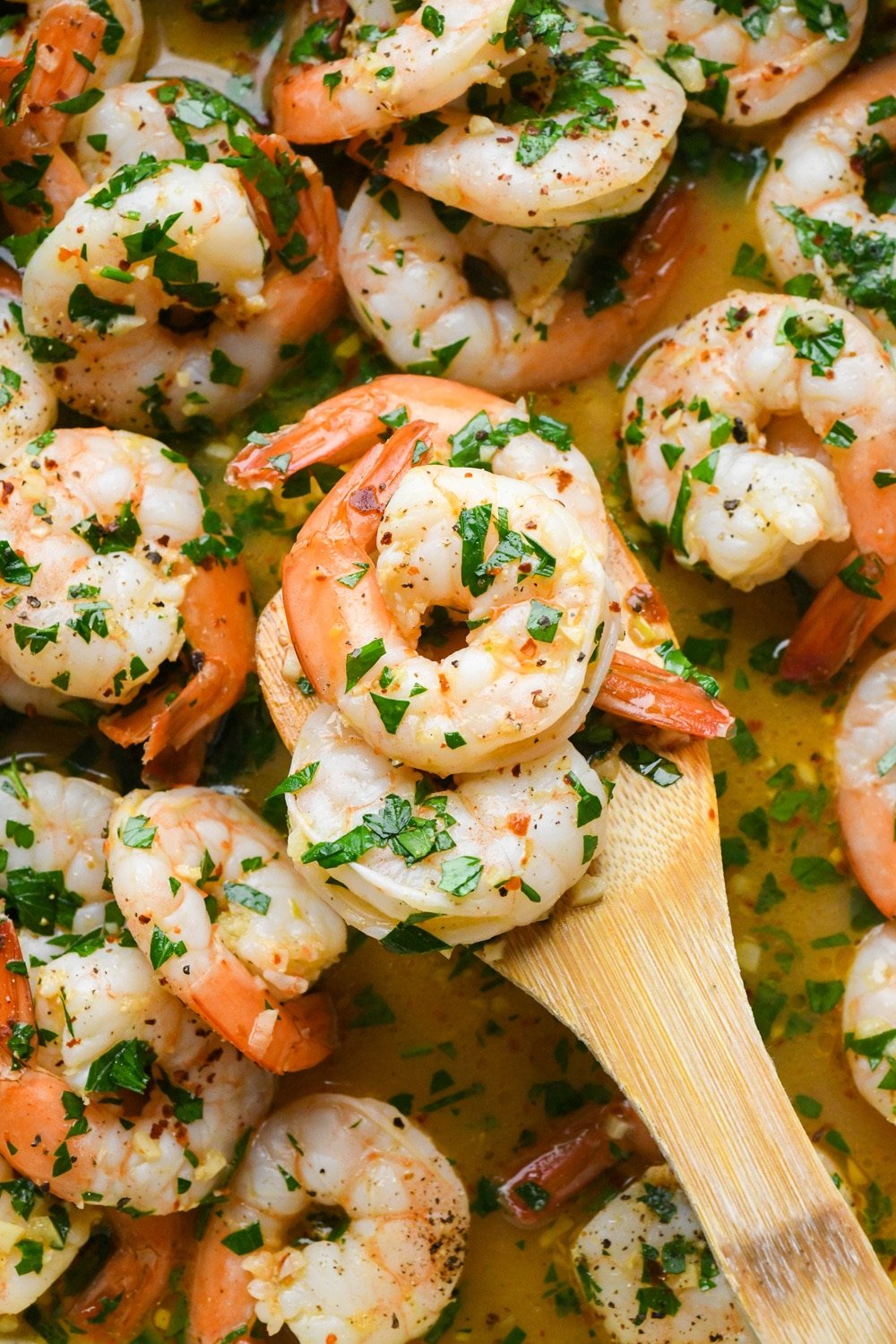 A wooden spatula lifting out several shrimp from prepared skillet of shrimp scampi.