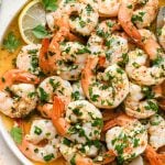 Cooked shrimp scampi without wine with parsley, lemon, and garlic, on a round platter.