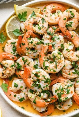 Cooked shrimp scampi without wine with parsley, lemon, and garlic, on a round platter.