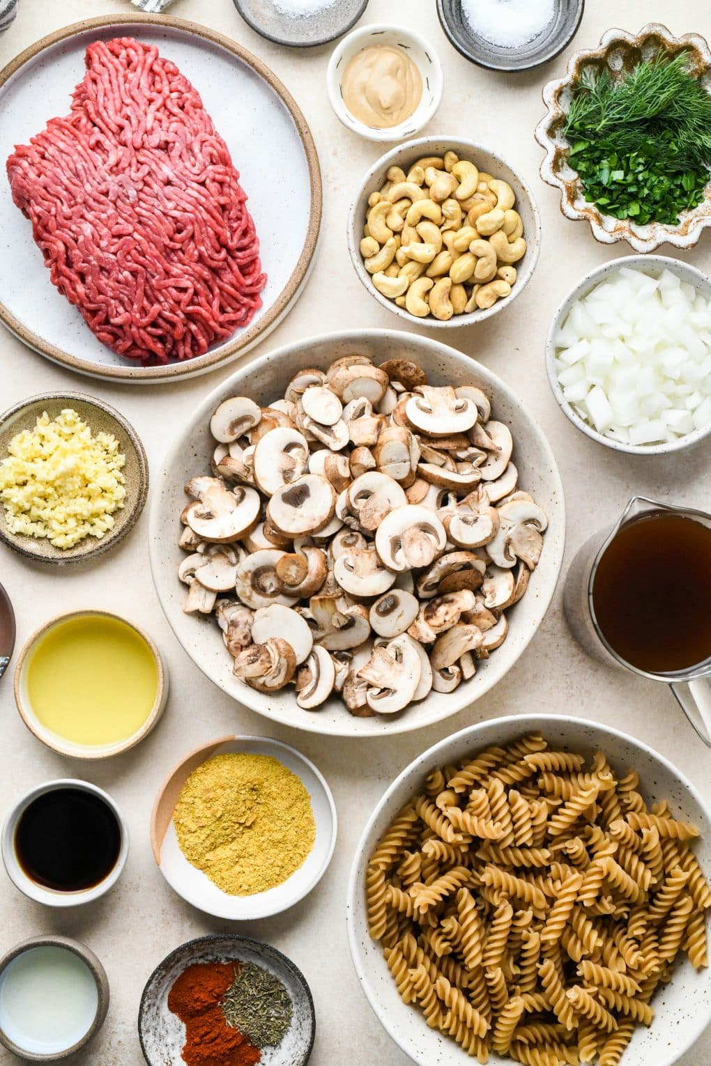Ingredients for dairy free beef stroganoff in various ceramic dishes on a cream colored background.