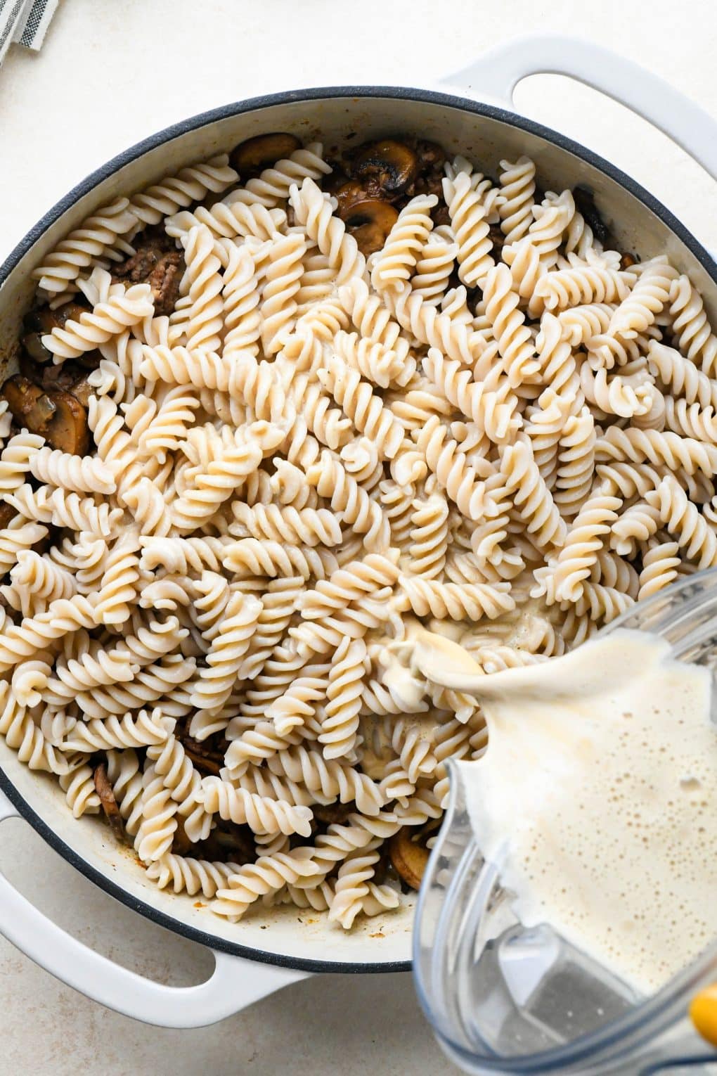 How to make Dairy Free Beef Stroganoff: Pouring the cashew cream sauce into the skillet with all of the pasta componenets.