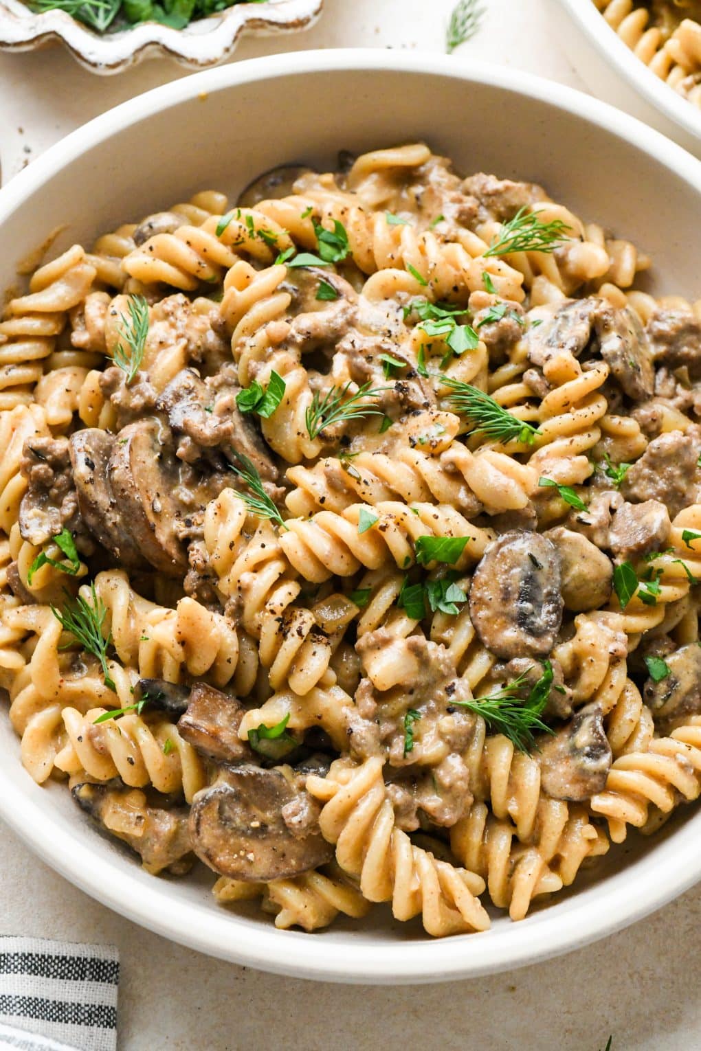 A shallow ceramic bowl of dairy free beef stroganoff with ground beef and mushrooms, garnished with fresh dill and fresh parsley.