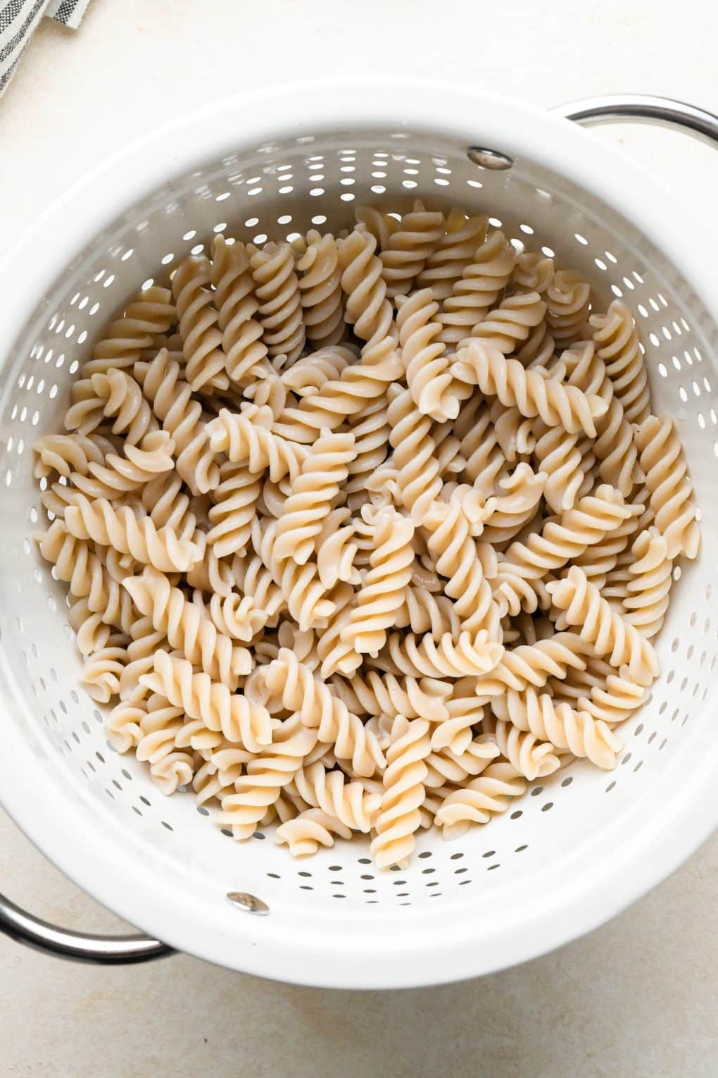 How to make Dairy Free Beef Stroganoff: Cooked gluten free fusili pasta strained in a white colander.