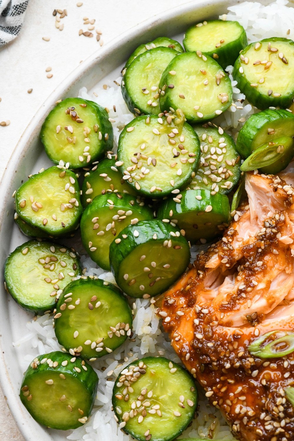Cucumber sesame salad on a plate with white rice and garlic ginger salmon.