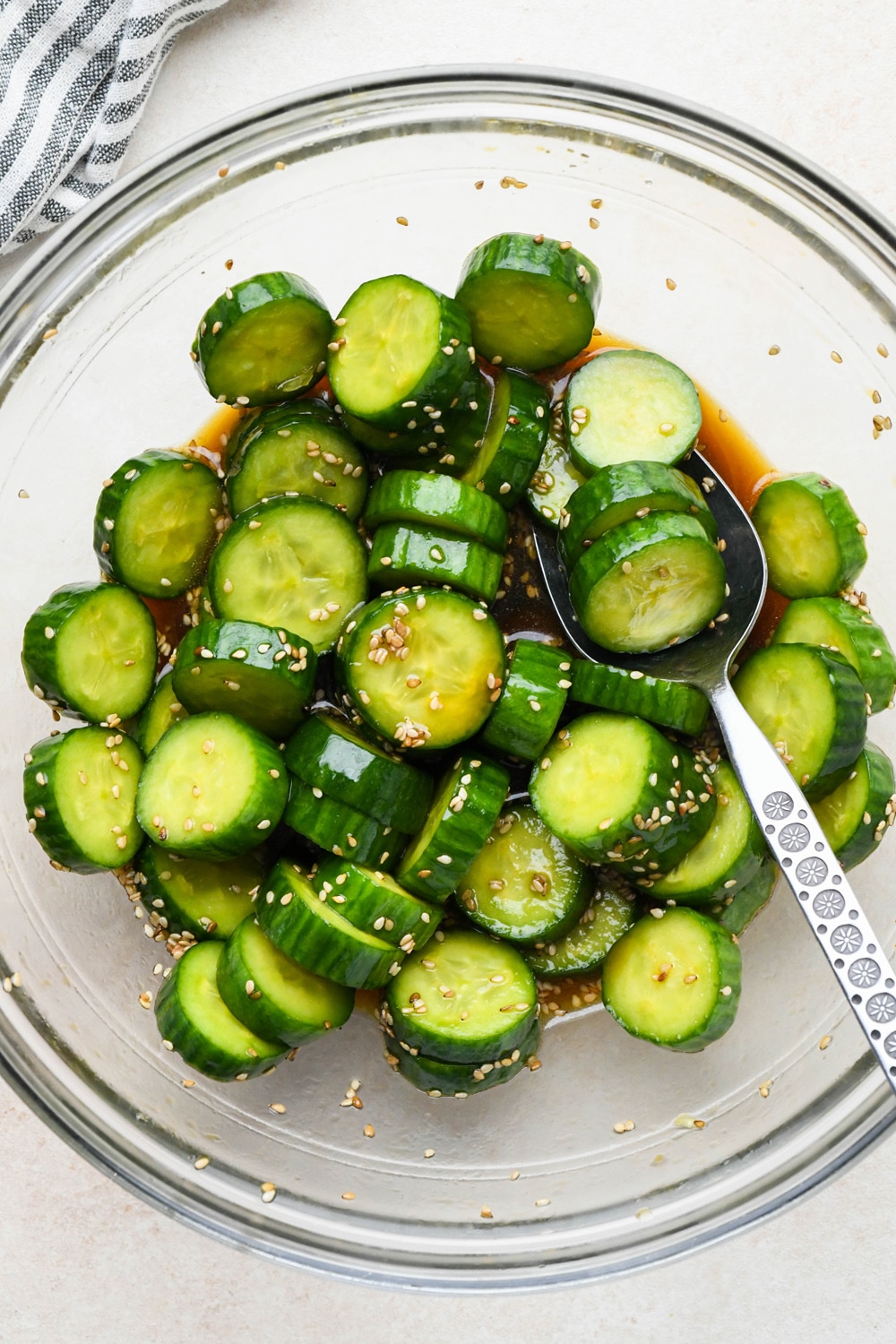 How to make cucumber sesame salad: Dressing poured over sliced cucumbers in a medium sized glass bowl, after marinating.
