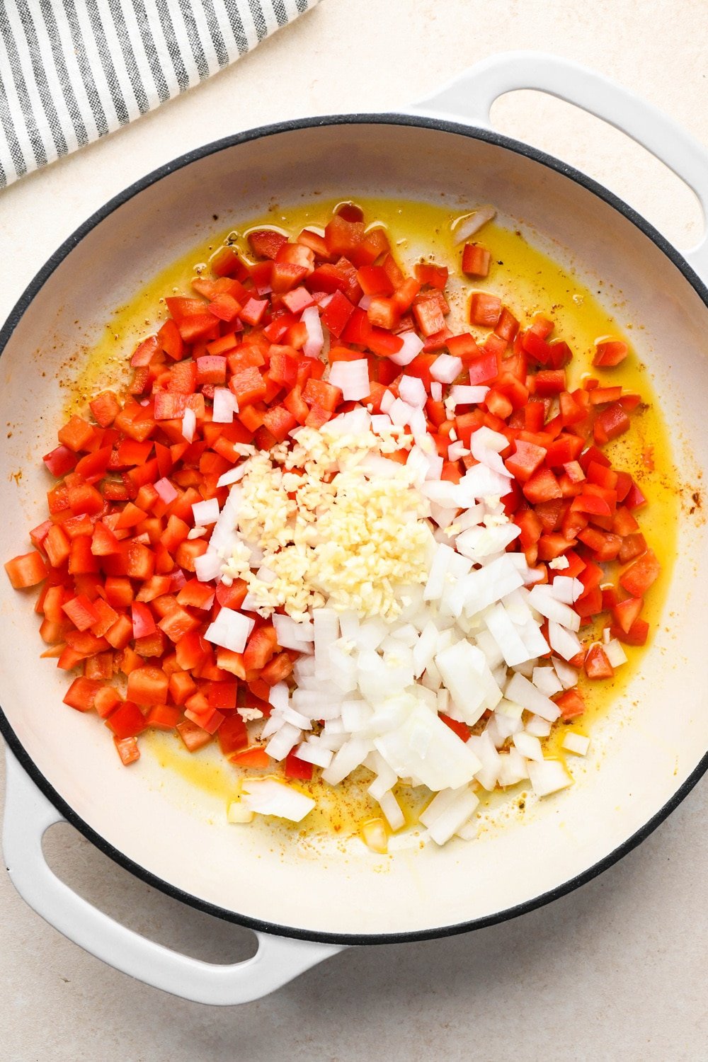 How to make curry chicken and rice: Raw diced red bell pepper, onions, and chopped garlic in a skillet with olive oil before sautéing. 