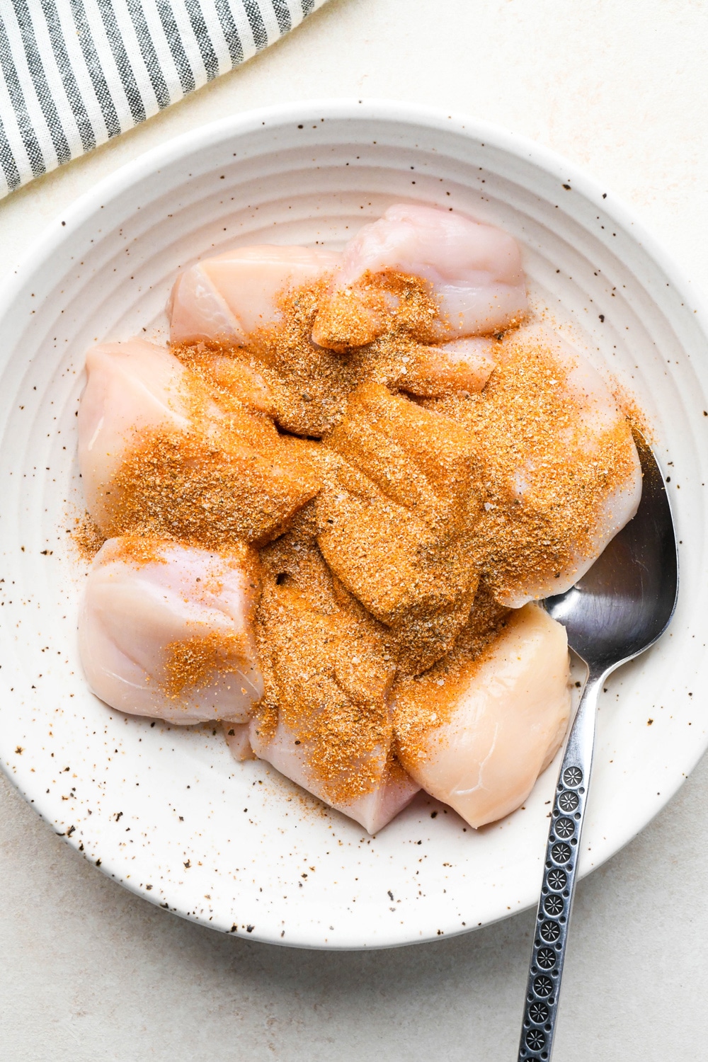 How to make curry chicken and rice: Spice mixture sprinkled over chicken breast pieces in a large ceramic bowl.