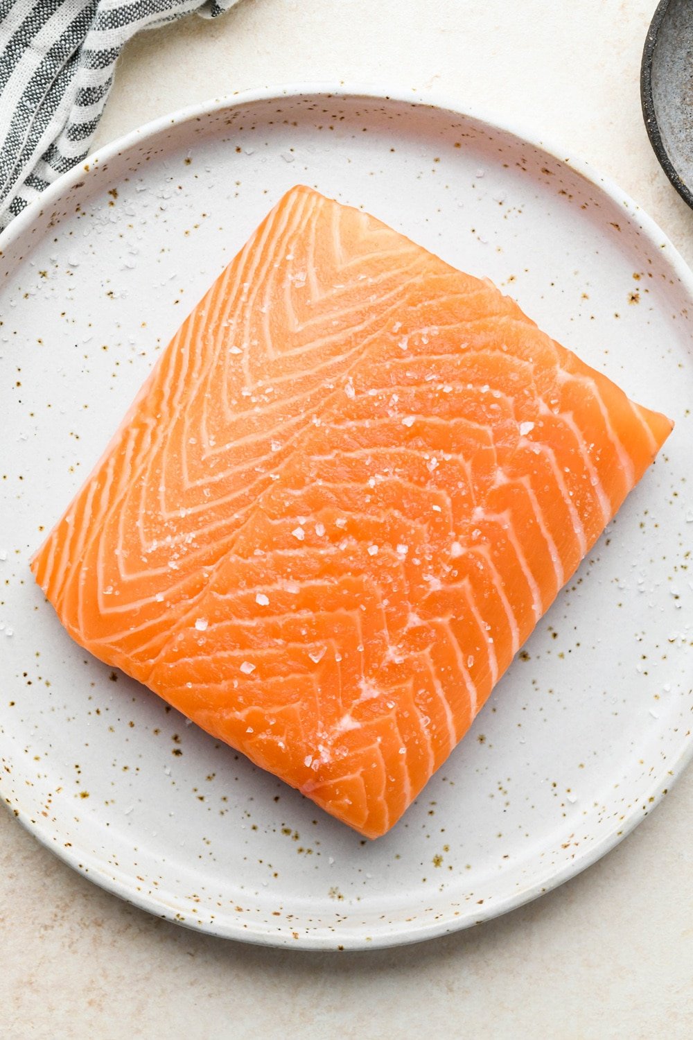 How to make garlic ginger salmon: Salmon filet patted dry on a small ceramic plate, topped with a sprinkle of kosher salt.