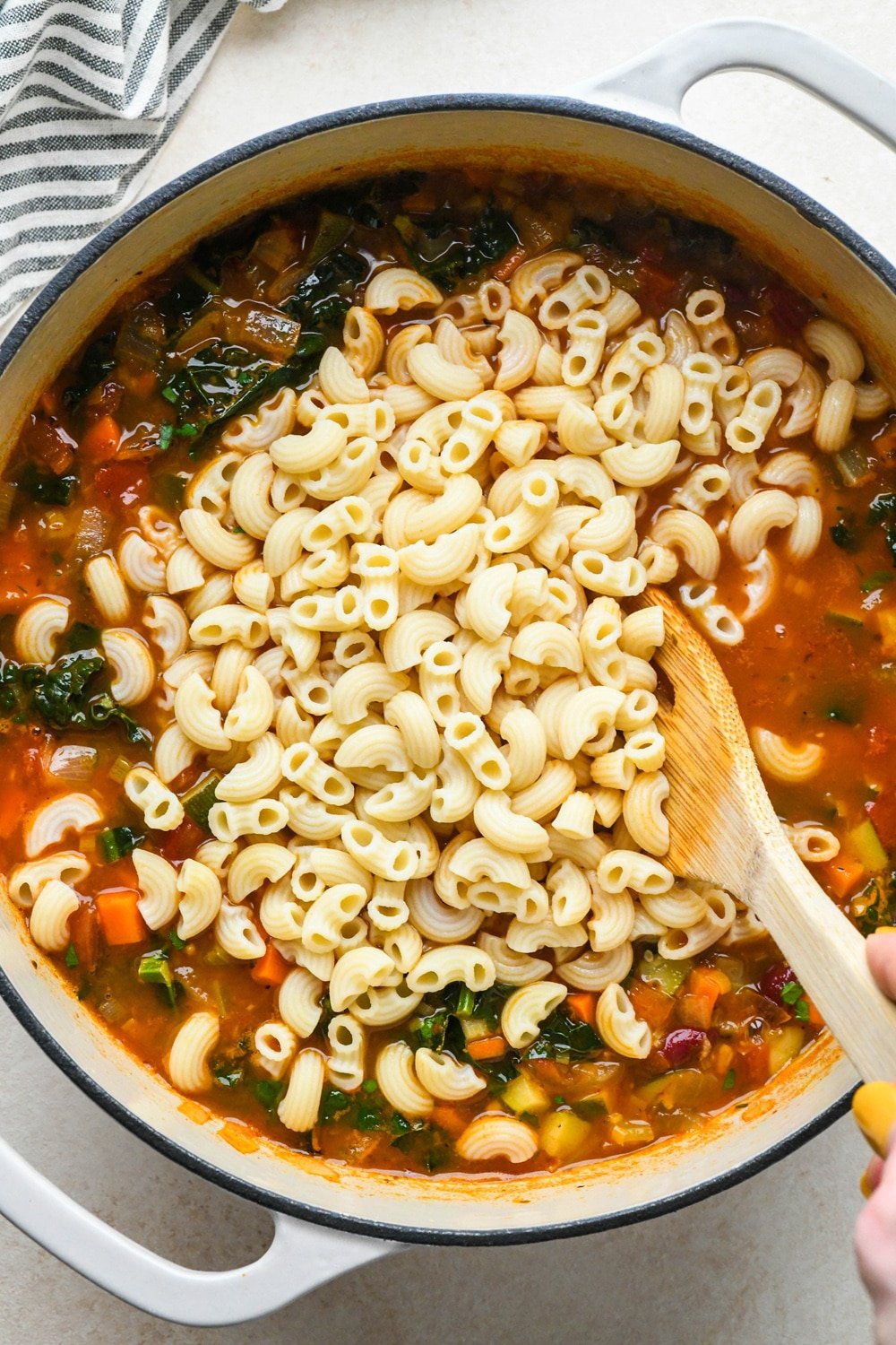 How to make Gluten Free Minestrone Soup: Cooked macaroni pasta added to soup before stirring to combine.