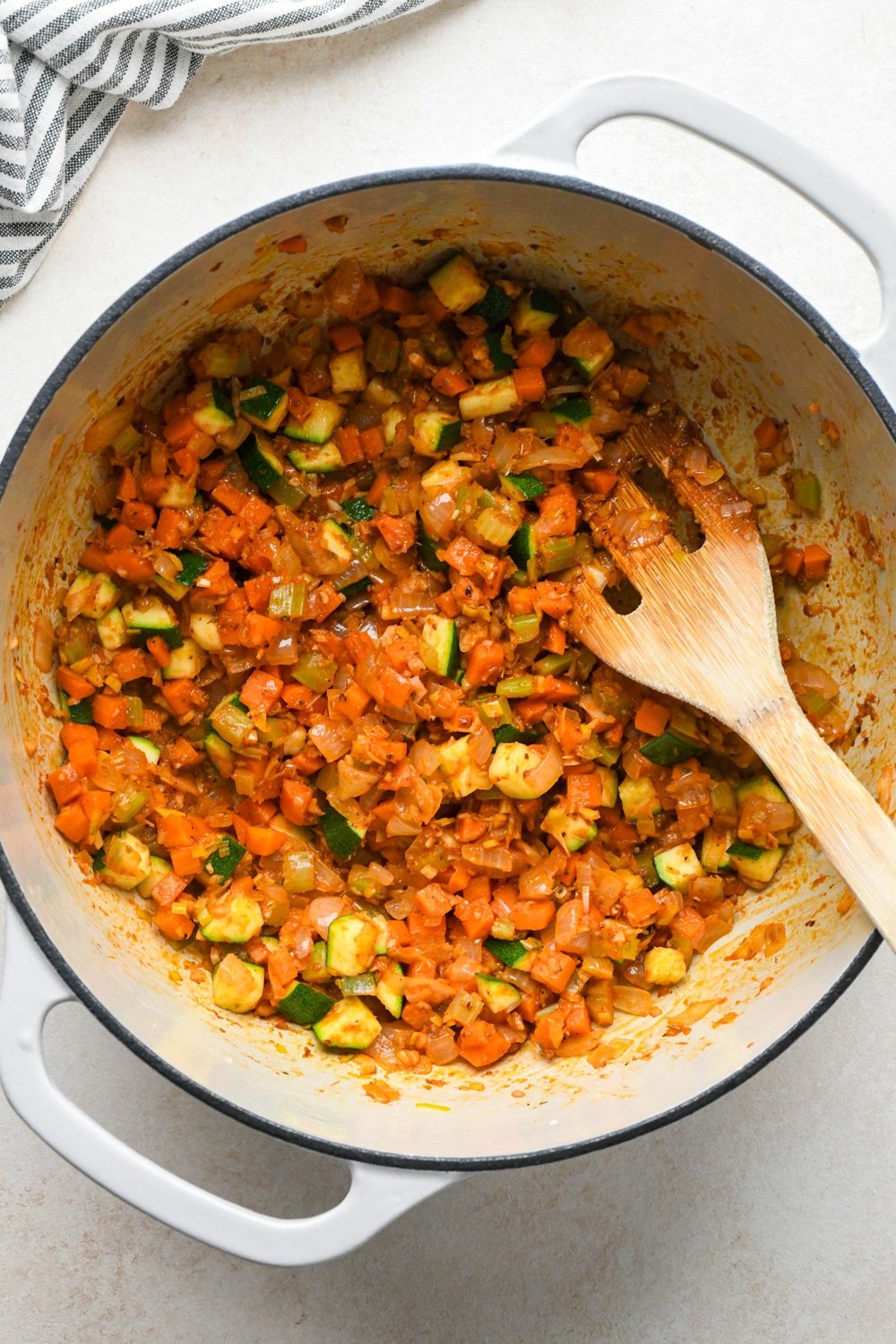 How to make Gluten Free Minestrone Soup: Diced zucchini, tomato paste, and dried spices added to the soup pot with sautéed vegetables, after stirring to combine and cooking until tomato paste has darkened.
