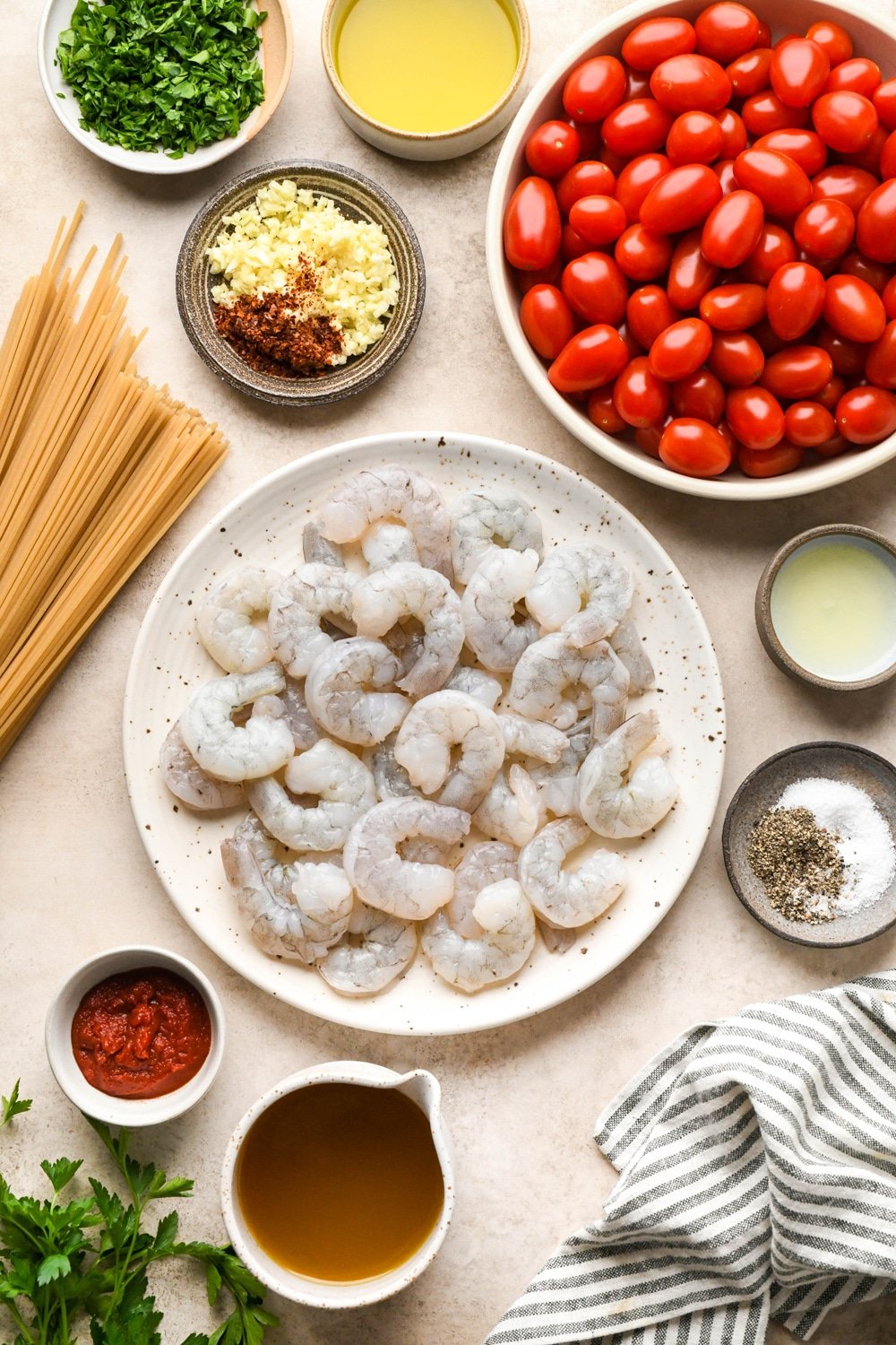 Ingredients for burst cherry tomato and shrimp pasta in various ceramics on a warm light brown background.