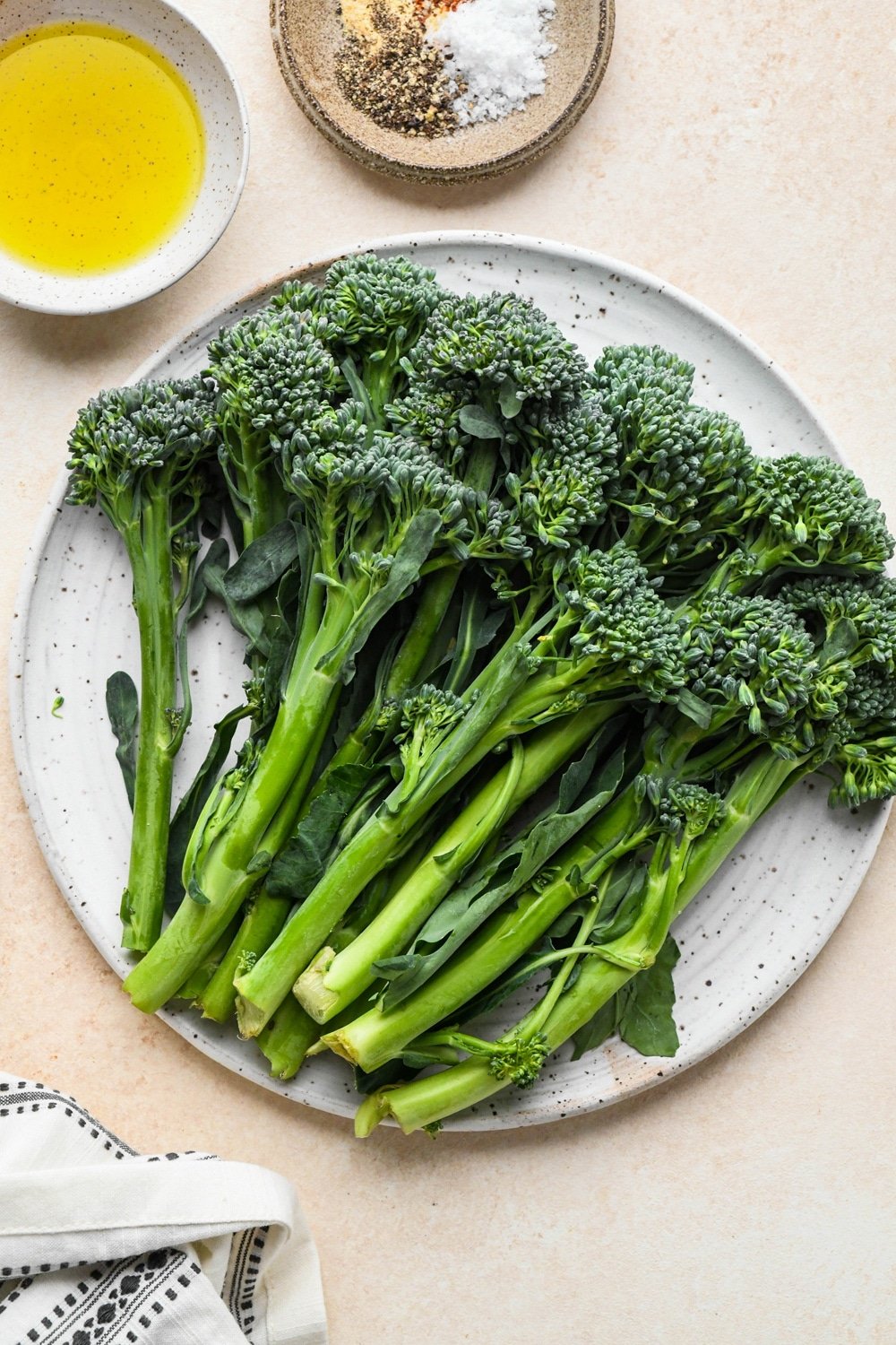 Ingredients for roasted broccolini in various ceramics on a cream colored background.