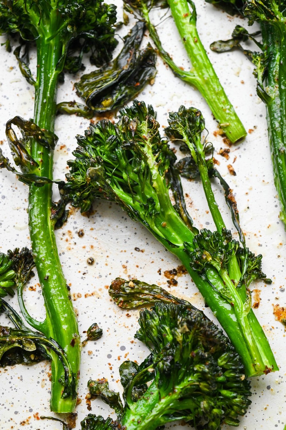 How to make roasted broccolini: Roasted broccolini stalks on sheet pan right after coming out of the oven. The broccolini is bright green with bits of charred pieces.