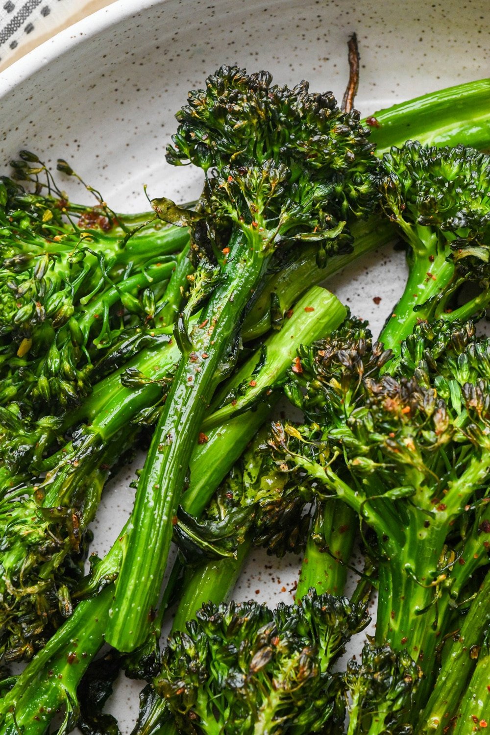 Close up of a stalk of roasted broccolini in a serving dish to show the nicely caramelized texture.