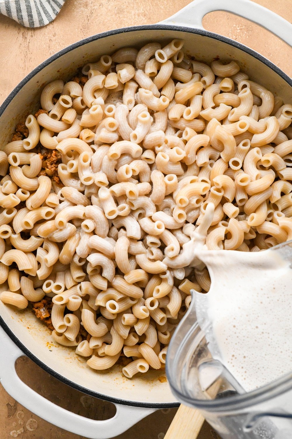 How to make dairy free hamburger helper: Cooked macaroni pasta and cashew cream sauce being added to the skillet with ground beef mixture.