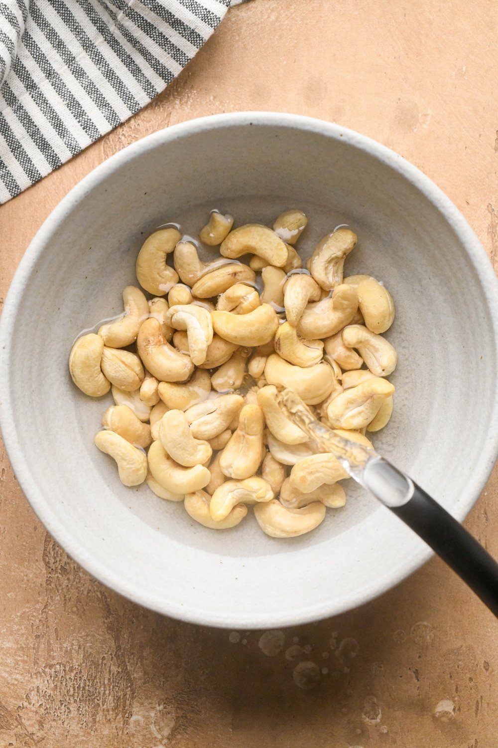 How to make dairy free hamburger helper: A hot water kettle pouring just boiled water into a heat proof grey ceramic bowl with raw cashews.