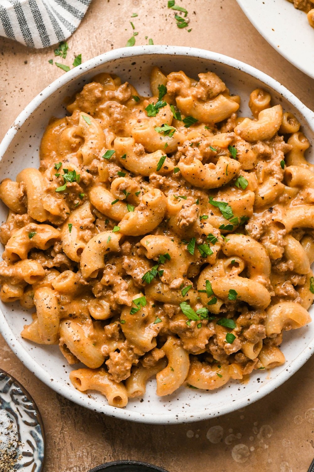 A shallow pasta bowl of gluten free and dairy free hamburger helper with macaroni noodles and ground beef in a rich creamy sauce, topped with fresh chopped parsley.