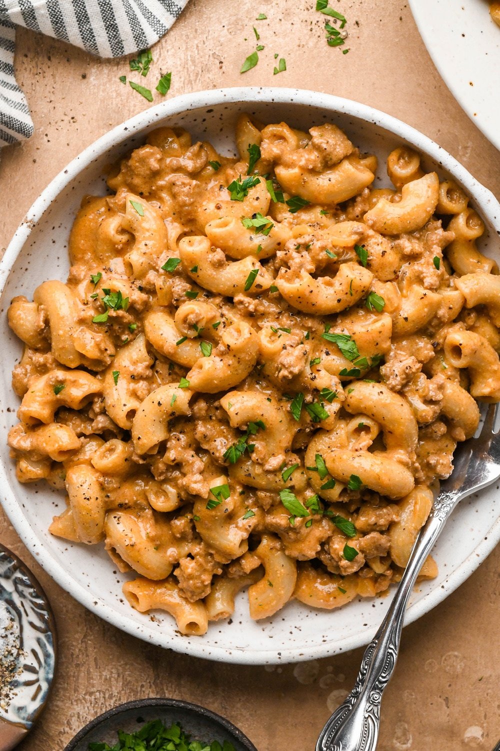 A shallow pasta bowl of gluten free and dairy free hamburger helper with macaroni noodles and ground beef in a rich creamy sauce, topped with fresh chopped parsley with a fork angled into the bowl.