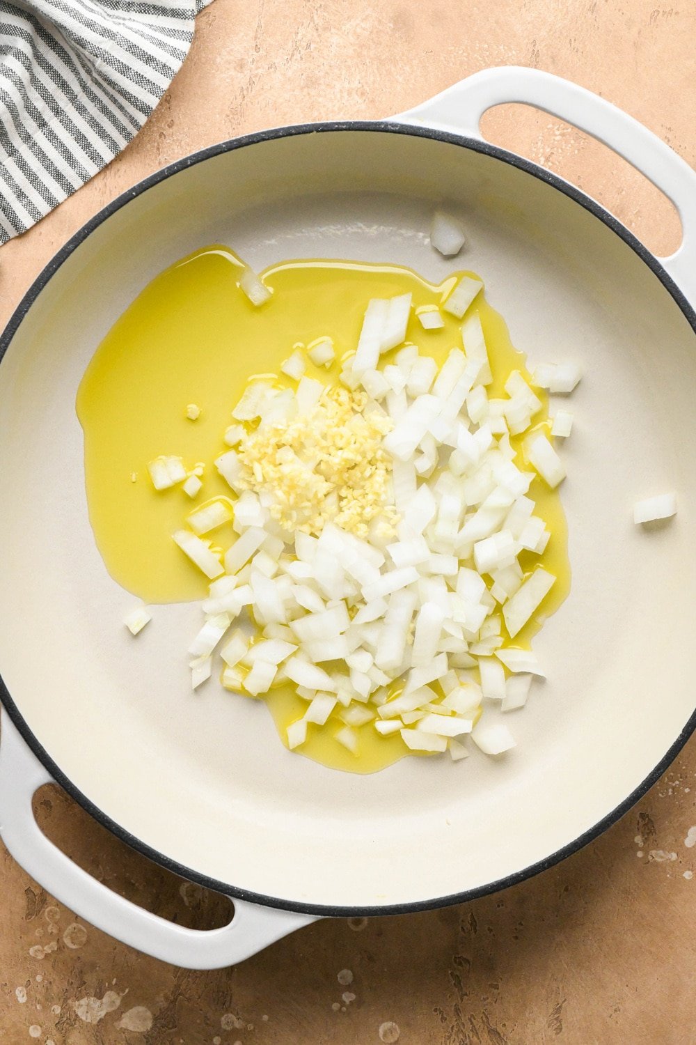 How to make dairy free hamburger helper: Olive oil, diced onions, and chopped garlic in a large white ceramic coated cast iron skillet - before sautéing. 