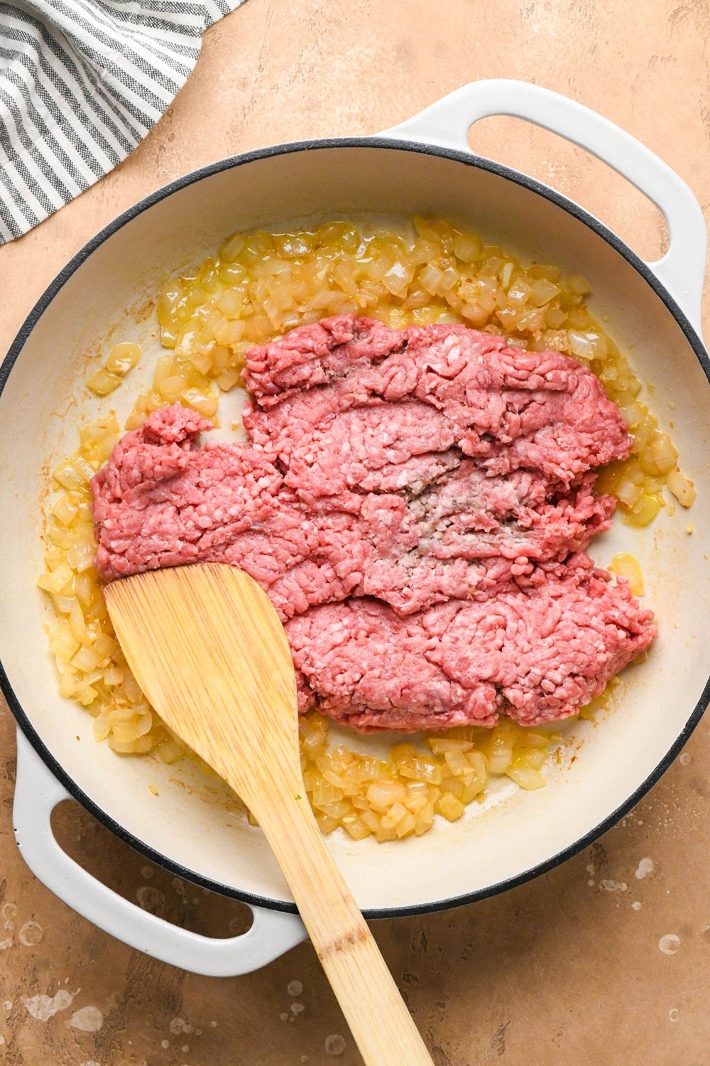 How to make dairy free hamburger helper: Olive oil, diced onions, and chopped garlic in a large white ceramic coated cast iron skillet - after sautéing until caramelized with ground beef added.