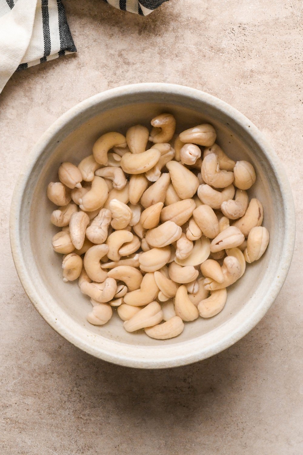 How to make dairy free tzatziki: Raw cashews in a grey ceramic bowl after soaking. Cashews are paler in color and plump.