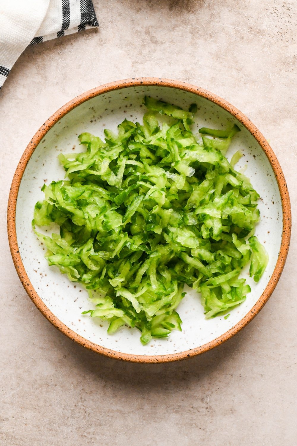 How to make dairy free tzatziki: A small ceramic speckled bowl of grated cucumber after all the excess moisture has been squeezed out.