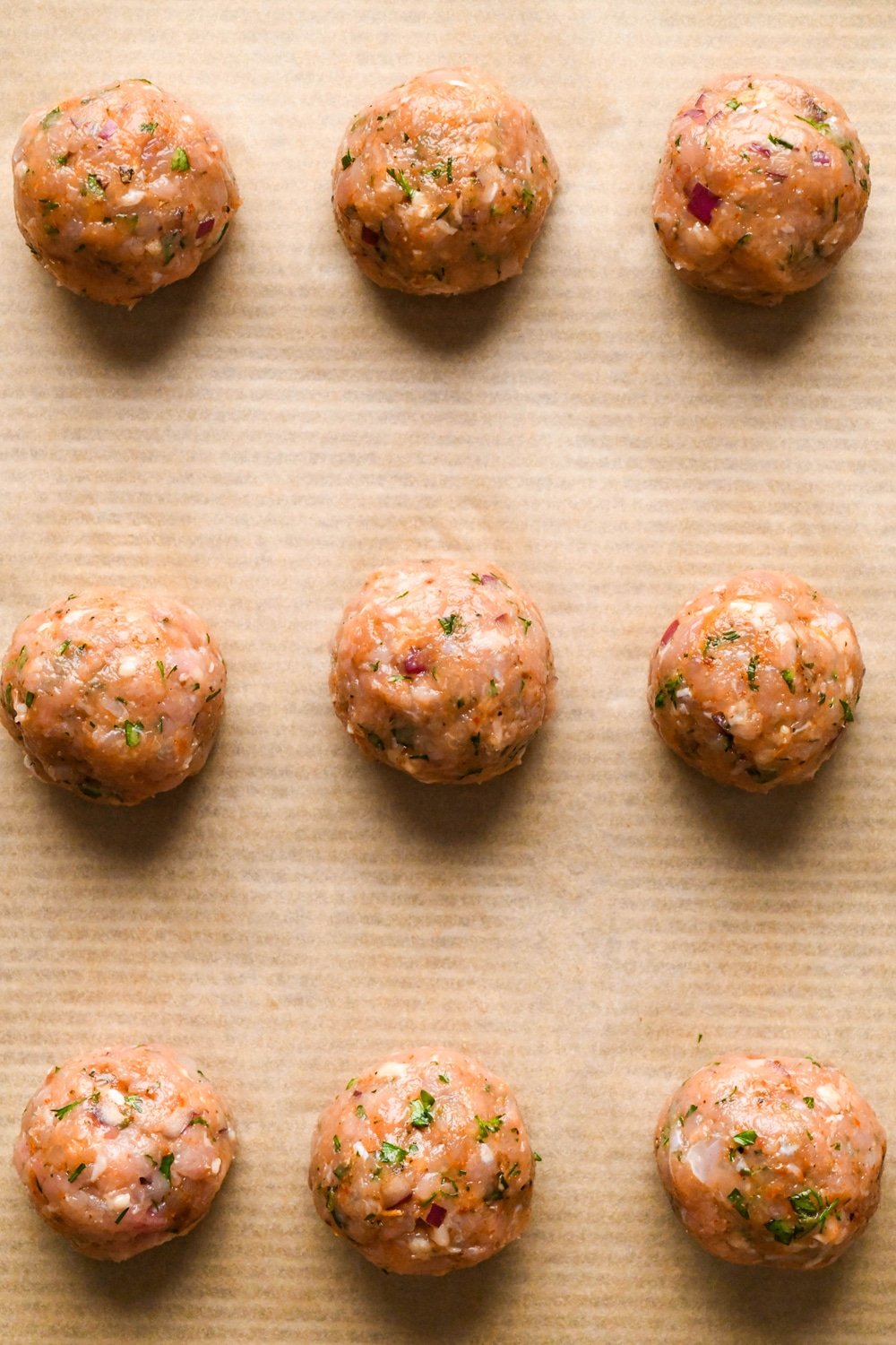 How to make Greek chicken meatballs: Meatballs evenly spaced on a parchment lined baking sheet before cooking.