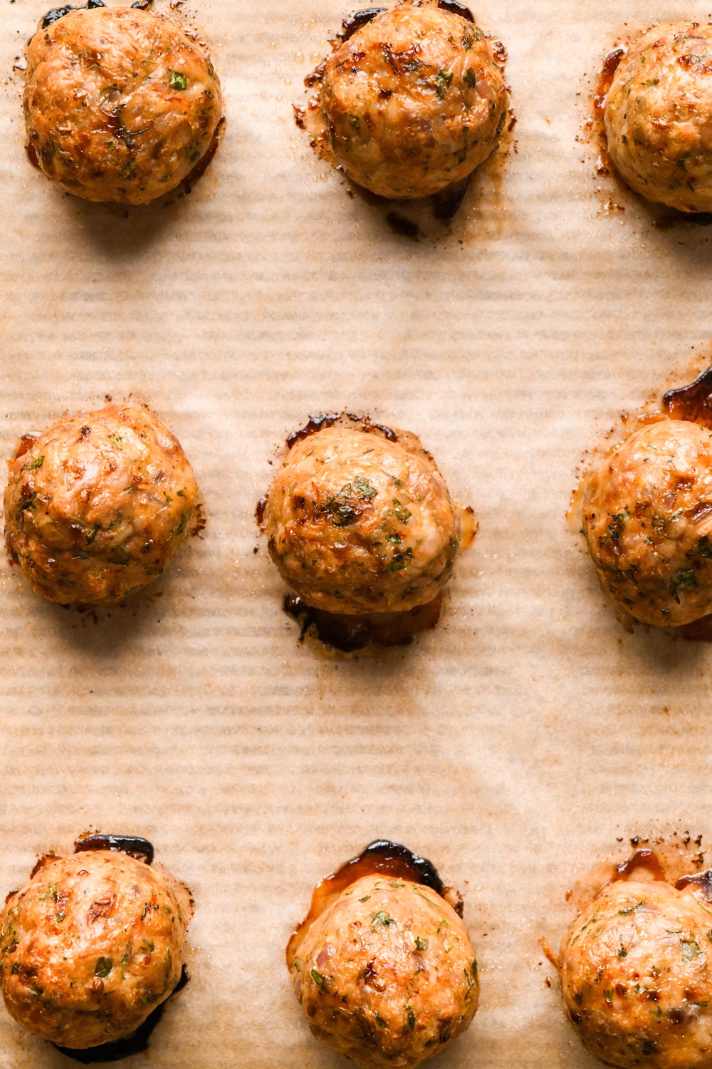 How to make Greek chicken meatballs: Meatballs evenly spaced on a parchment lined baking sheet after cooking. They are golden brown and juicy looking.