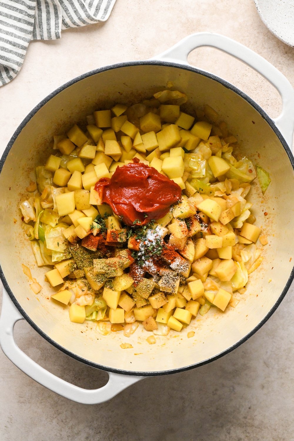 How to make Brothy Sausage and Potato Soup with Kale and Cabbage: Diced potatoes, tomato paste, spices, and herbs added to the pot with cabbage and onions. 