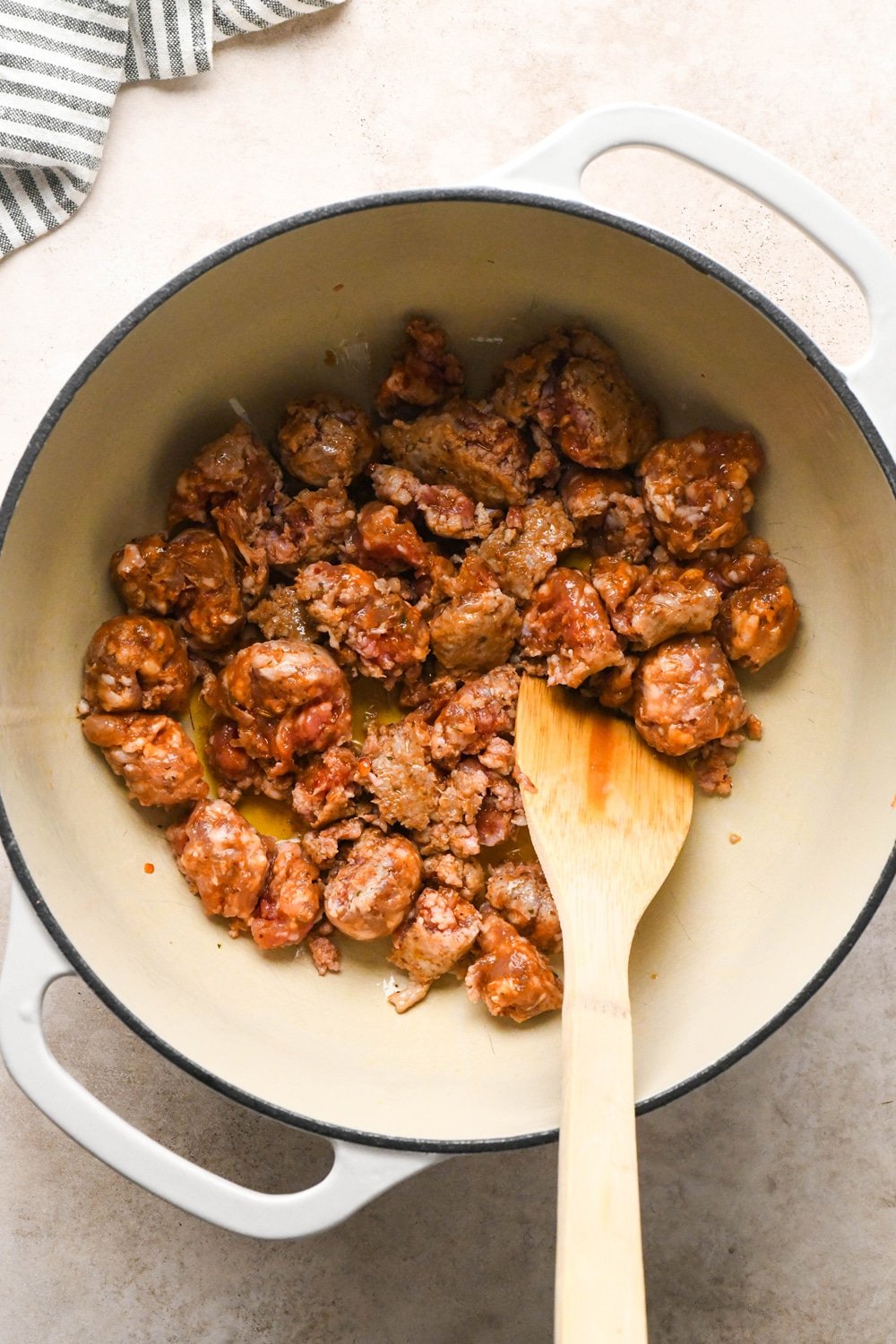 How to make Brothy Sausage and Potato Soup with Kale and Cabbage: Sausages in pot during cooking, breaking up with a spatula.