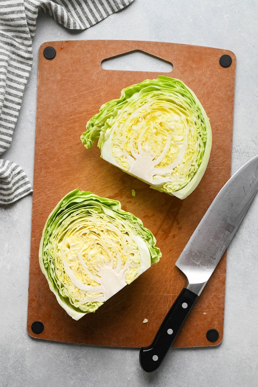 How to make chopped green cabbage salad: Step-by-step showing how to roughly chop cabbage. Small head of green cabbage is cut in half on a cutting board.