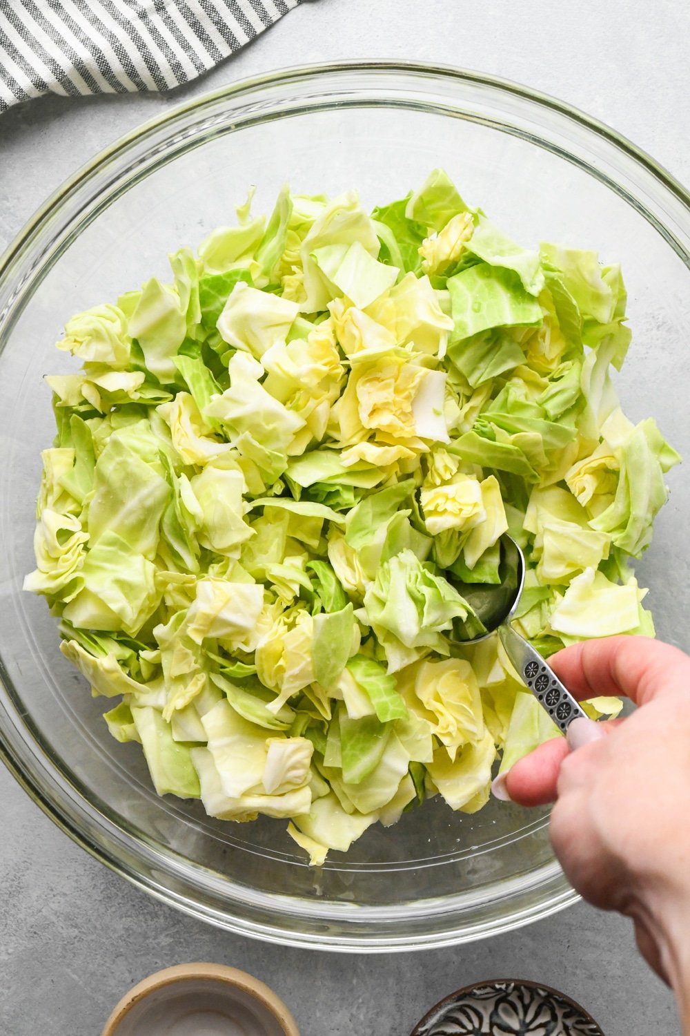 How to make chopped green cabbage salad: Cabbage being tossed together with salt and vinegar using a large metal spoon.