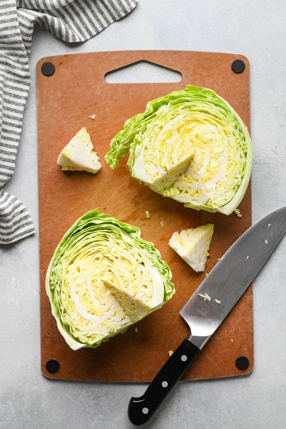 How to make chopped green cabbage salad: Step-by-step showing how to roughly chop cabbage. Small head of green cabbage is cut in half on a cutting board, and the stem is cut out of each side.