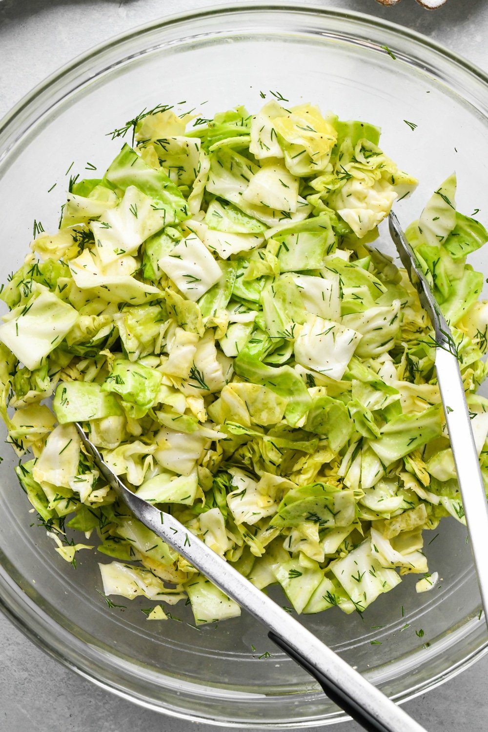 How to make chopped green cabbage salad: Salad after tossing together in a large glass bowl with kitchen tongs angled into the bowl. 