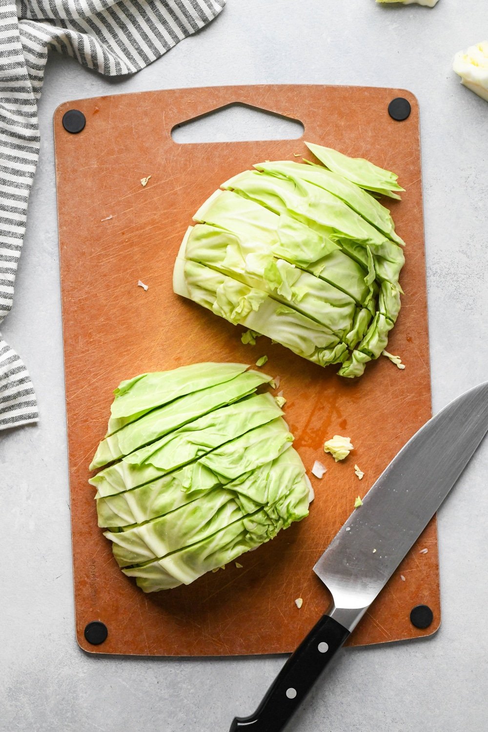 How to make chopped green cabbage salad: Step-by-step showing how to roughly chop cabbage. Small head of green cabbage is cut in half on a cutting board, facing flat side down and cabbage is cut into half inch thick strips.