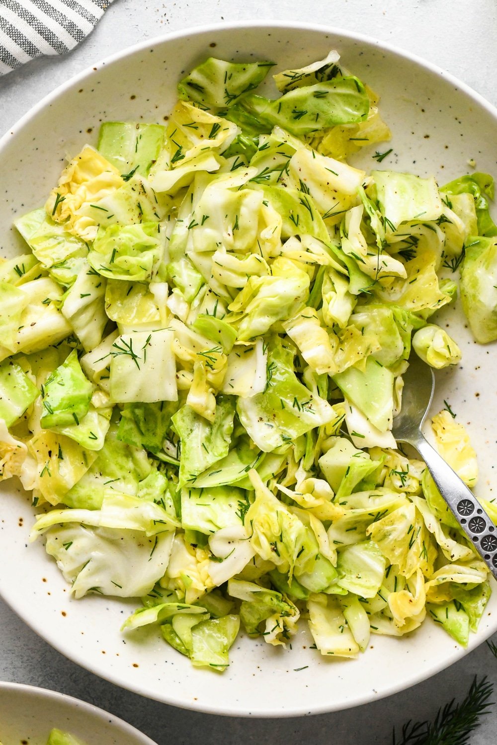 Chopped green cabbage salad with fresh dill in a serving bowl with a portion of the salad scooped out, and a spoon angled into the bowl. 