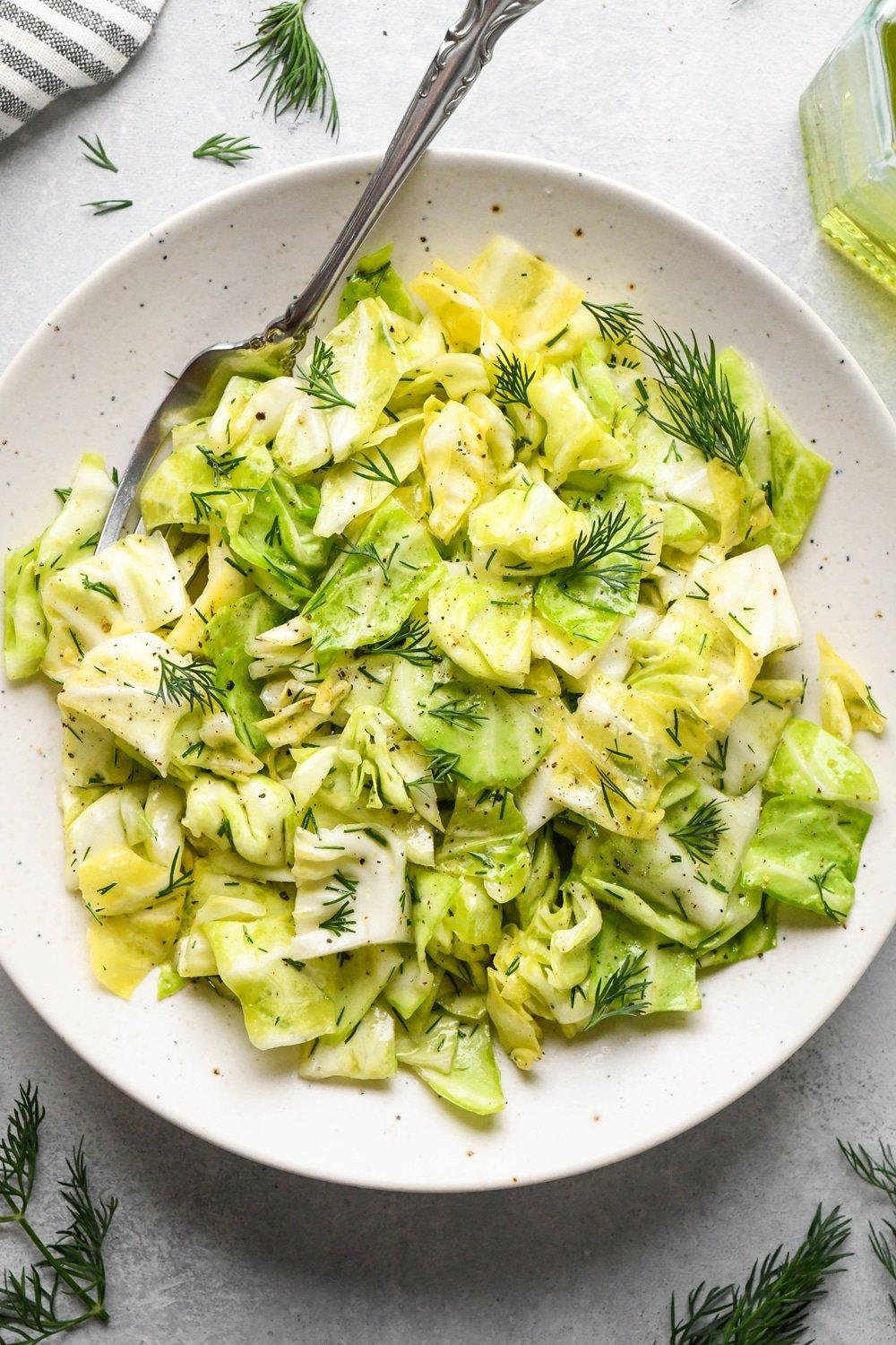 Chopped green cabbage salad in a small salad dish, with a fork angled onto the plate. The salad is garnished with chopped fresh dill.