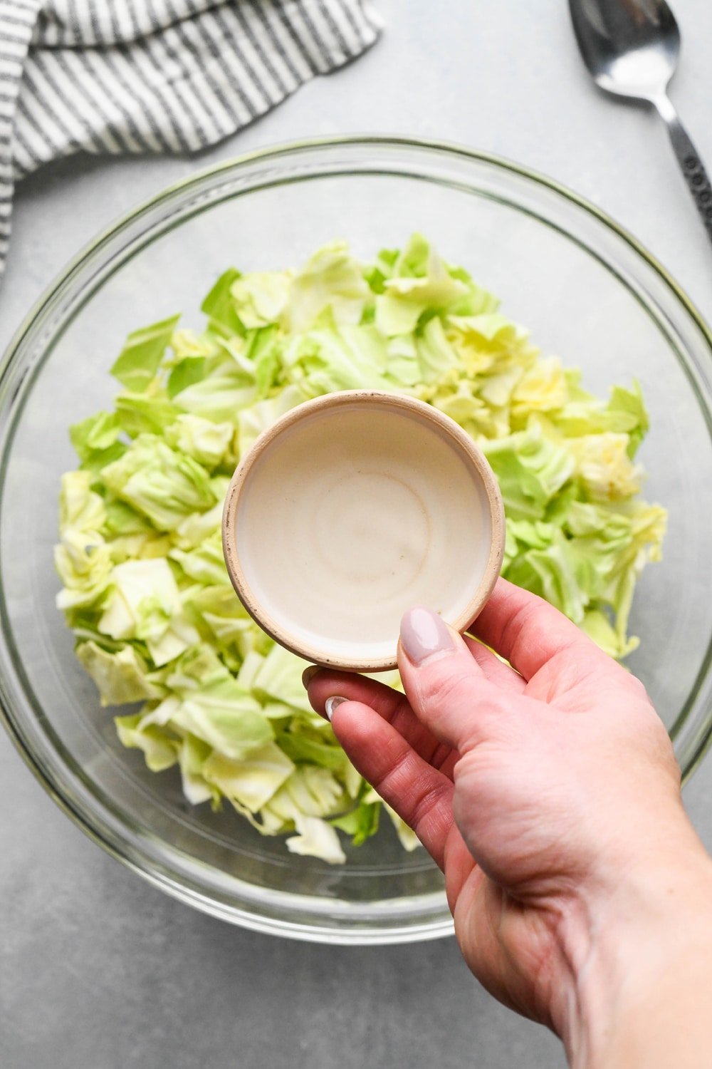 How to make chopped green cabbage salad: A hand adding rice vinegar from a small ceramic dish to the bowl of cabbage. 