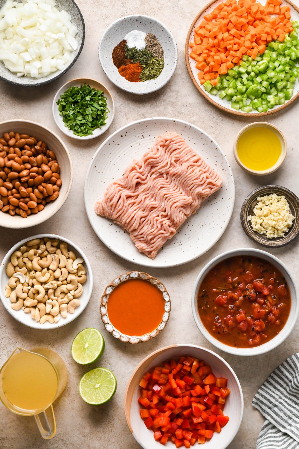 Ingredients for buffalo chicken chili on various ceramics on a light brown background.