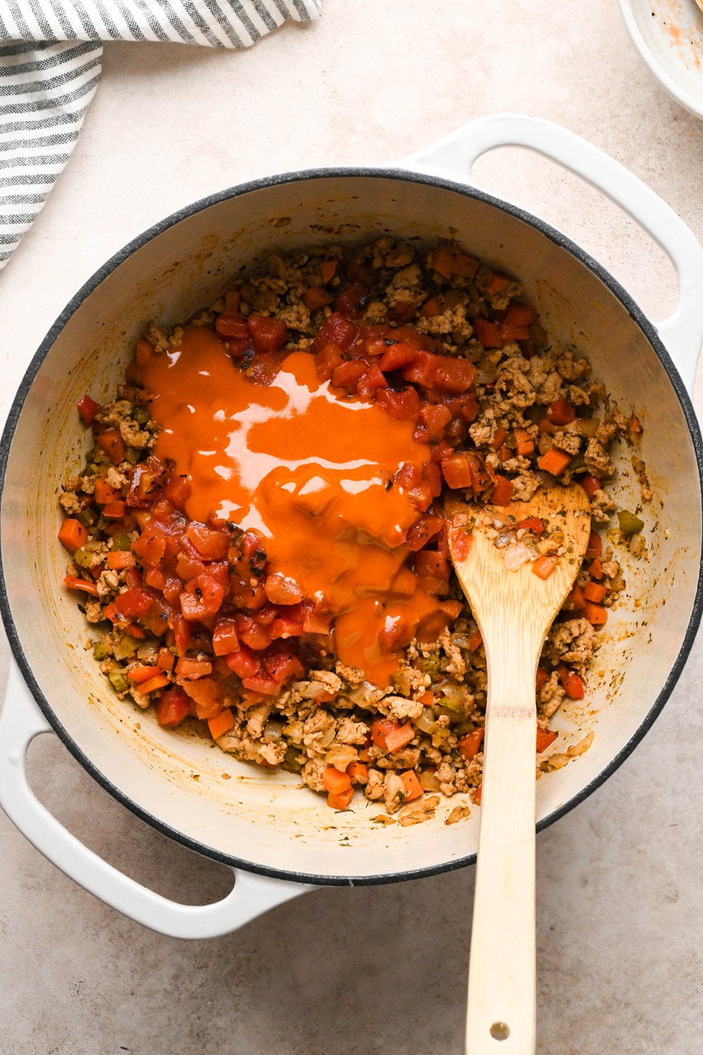 How to make Cashew Cream Buffalo Chicken Chili Made with Ground Chicken: Diced fire roasted tomatoes and buffalo sauce added to the soup pot with chicken, veggies, and spices, before stirring together.