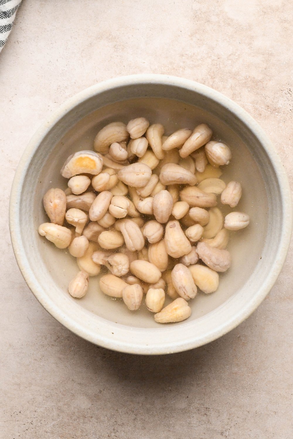 How to make Cashew Cream Buffalo Chicken Chili Made with Ground Chicken: Cashew in a grey ceramic bowl after soaking. They appear plump and are paler in color.