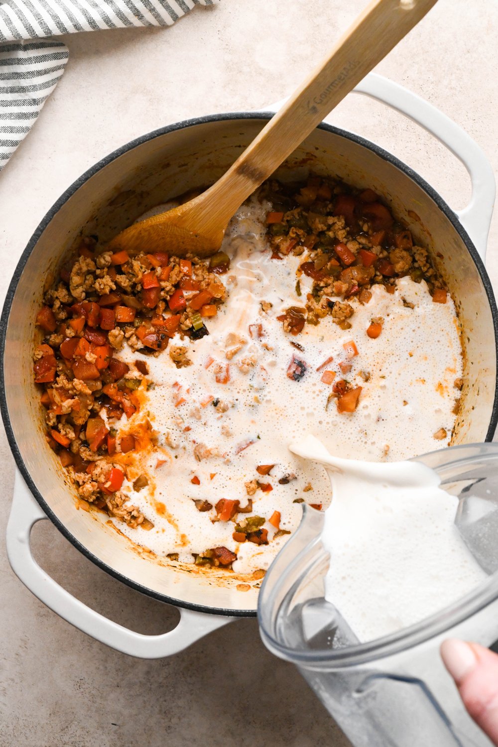 How to make Cashew Cream Buffalo Chicken Chili Made with Ground Chicken: Pouring blended cashew cream into the pot of soup. 