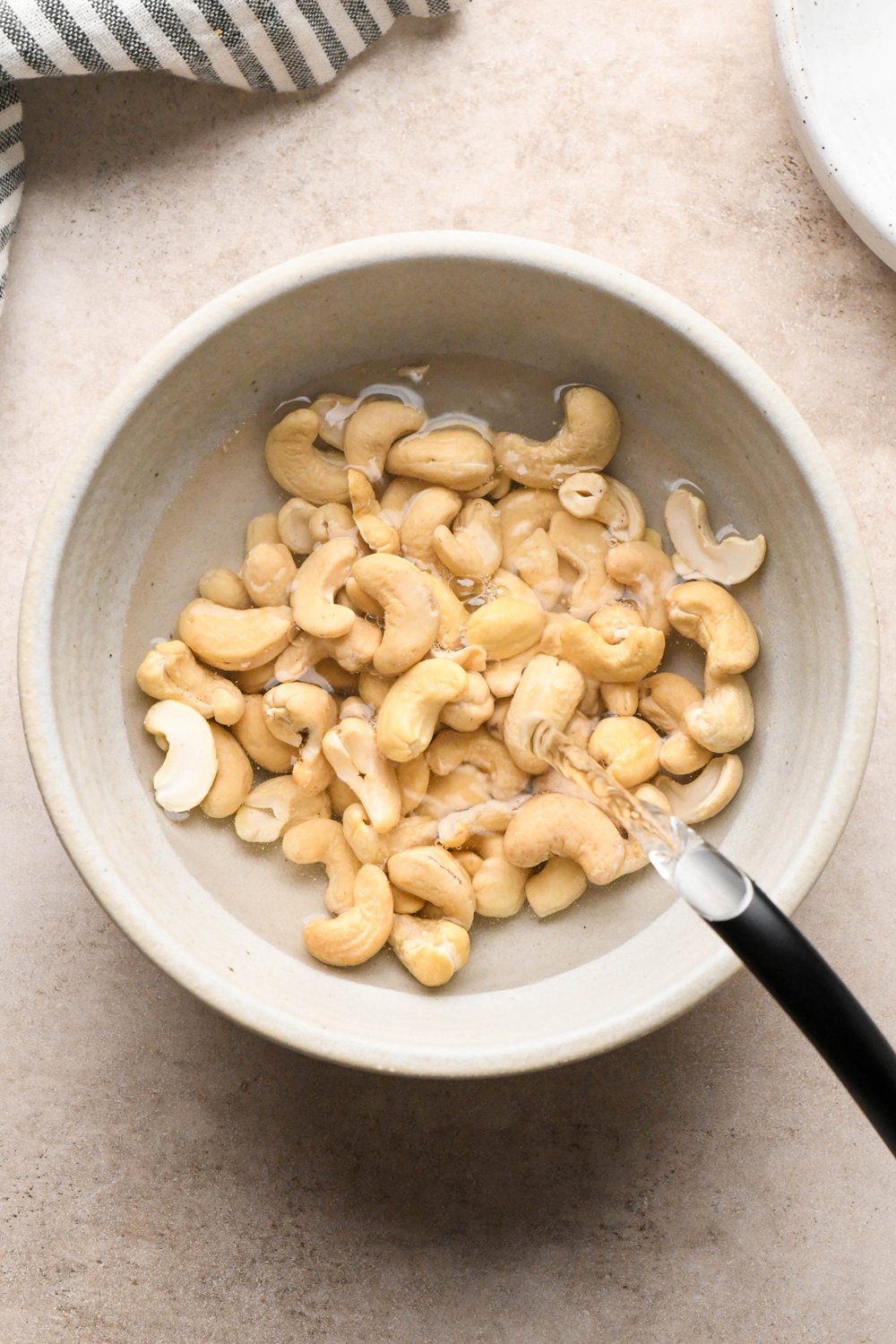 How to make Cashew Cream Buffalo Chicken Chili Made with Ground Chicken: Pouring hot water over raw cashews in a grey ceramic bowl so they can soak and soften.