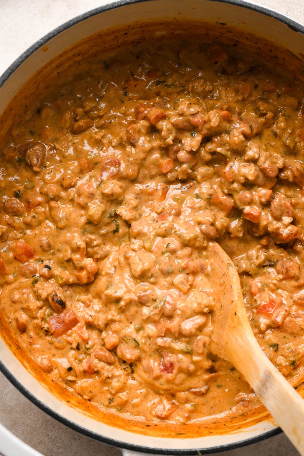 How to make Cashew Cream Buffalo Chicken Chili Made with Ground Chicken: Cashew cream in the pot of soup with drained beans and chopped cilantro stirred into the soup, after simmering to thicken, with a wooden spatula stirring the soup to show the thick and creamy texture.