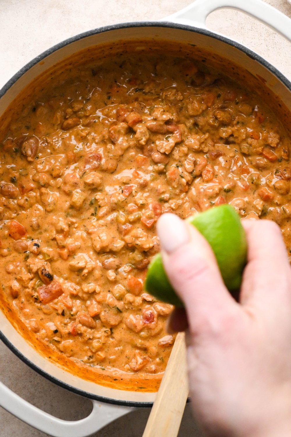 How to make Cashew Cream Buffalo Chicken Chili Made with Ground Chicken: A hand squeezing half a lime into the pot of soup.