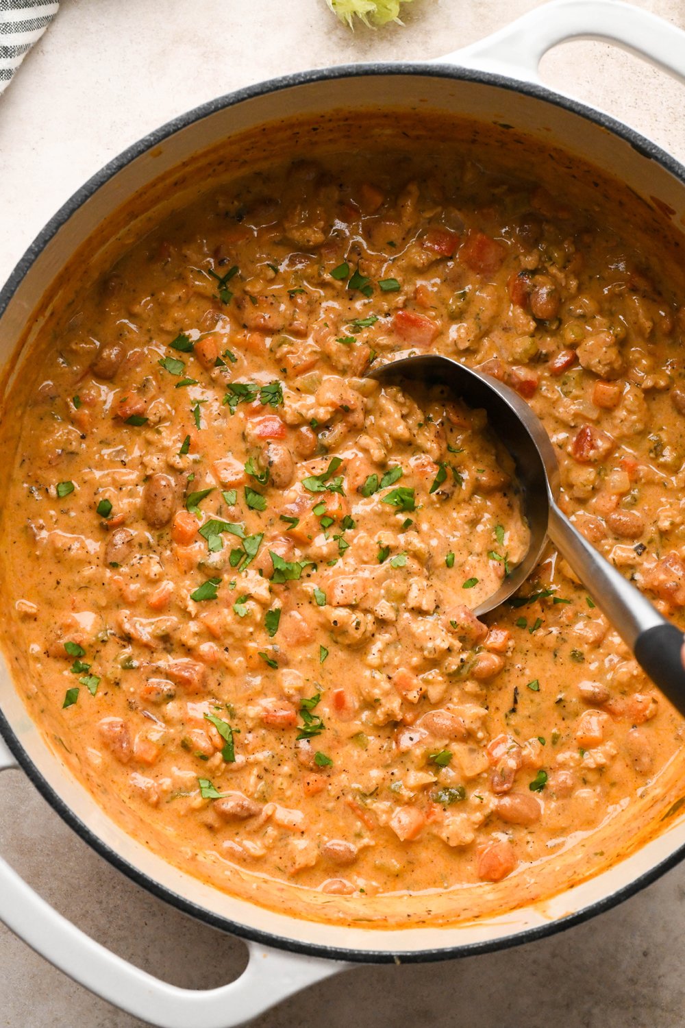 Cashew cream buffalo chicken chili in a large enameled off-white soup pot, garnished with chopped cilantro with a soup ladle dipping into the soup to show the hearty and creamy texture.