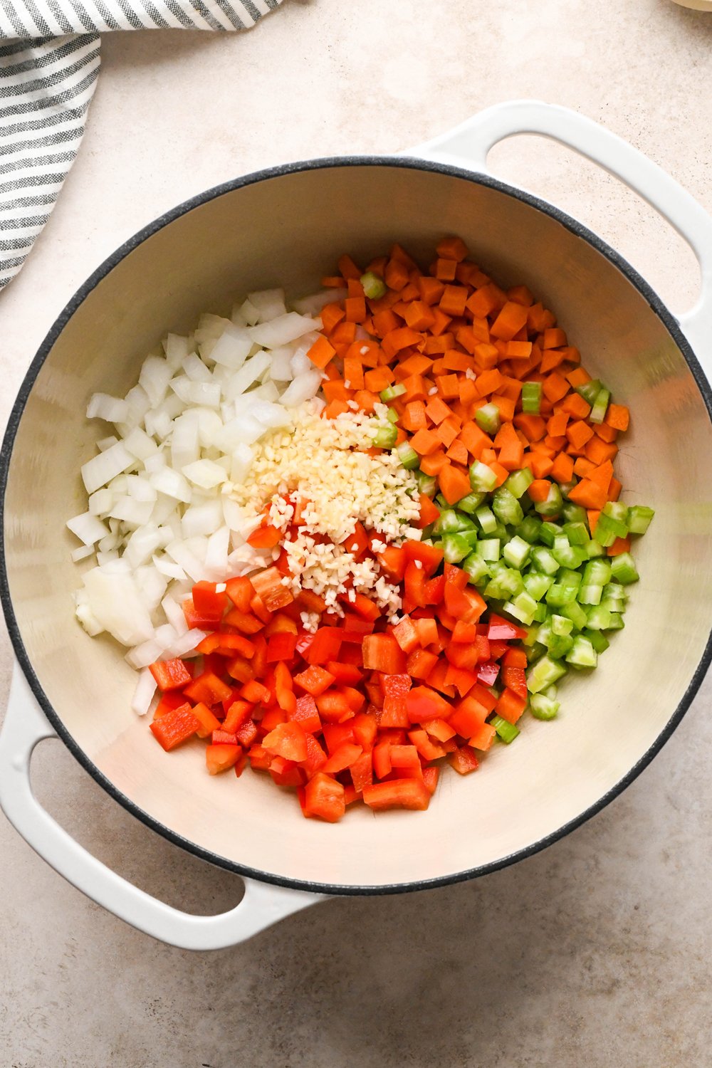 How to make Cashew Cream Buffalo Chicken Chili Made with Ground Chicken: Raw diced onion, carrots, celery, bell pepper, and garlic in a soup pot with olive oil before cooking.