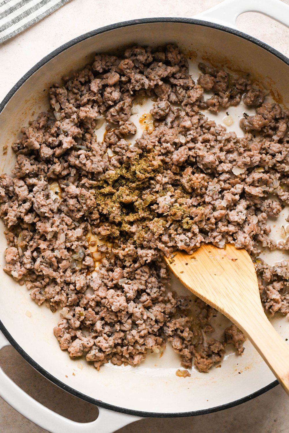 How to make Gluten Free Sausage Gravy: A spatula stirring all-purpose seasoning and coconut aminos into the cooked sausage and onions.